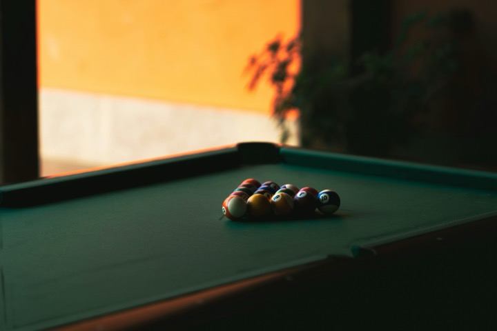 A player leans over a pool table at night, lining up a shot
