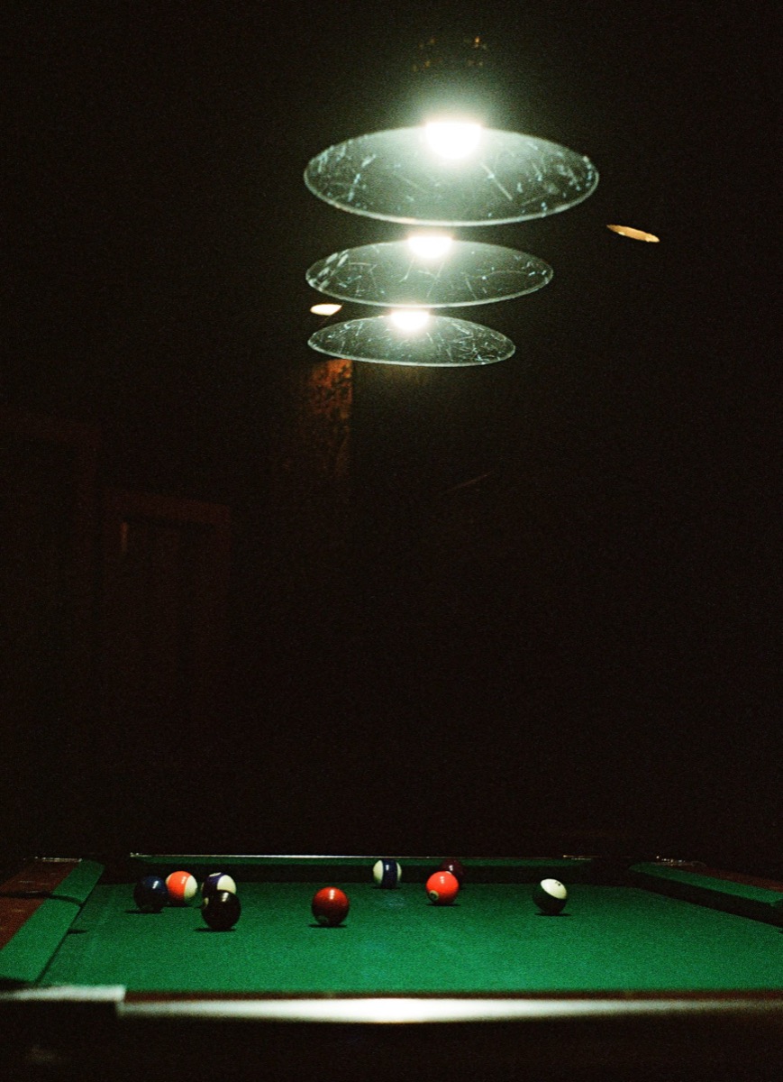 A racked set of balls on a green pool table in front of a sunlit orange wall