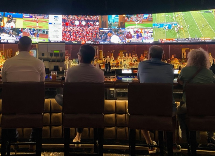 Fans seated at a bar beneath a wall of screens showing several live games