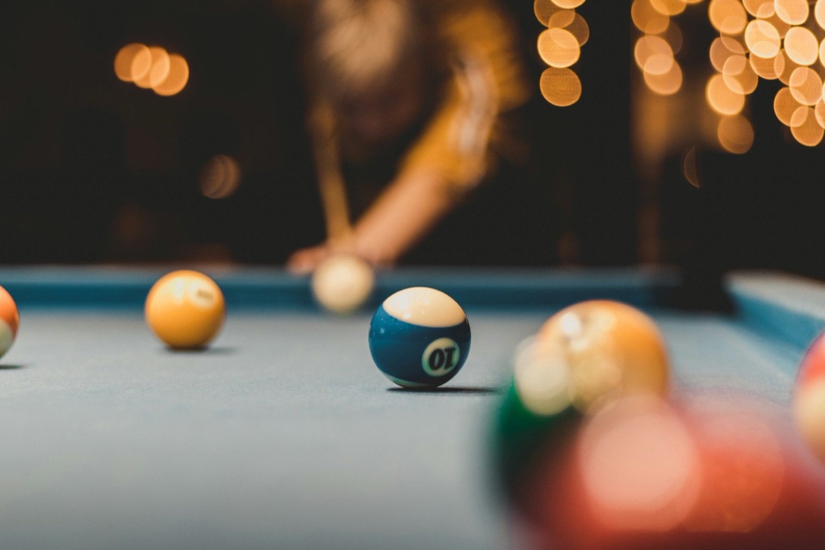 Close-up of a blue ten ball on a pool table with warm string lights blurred behind